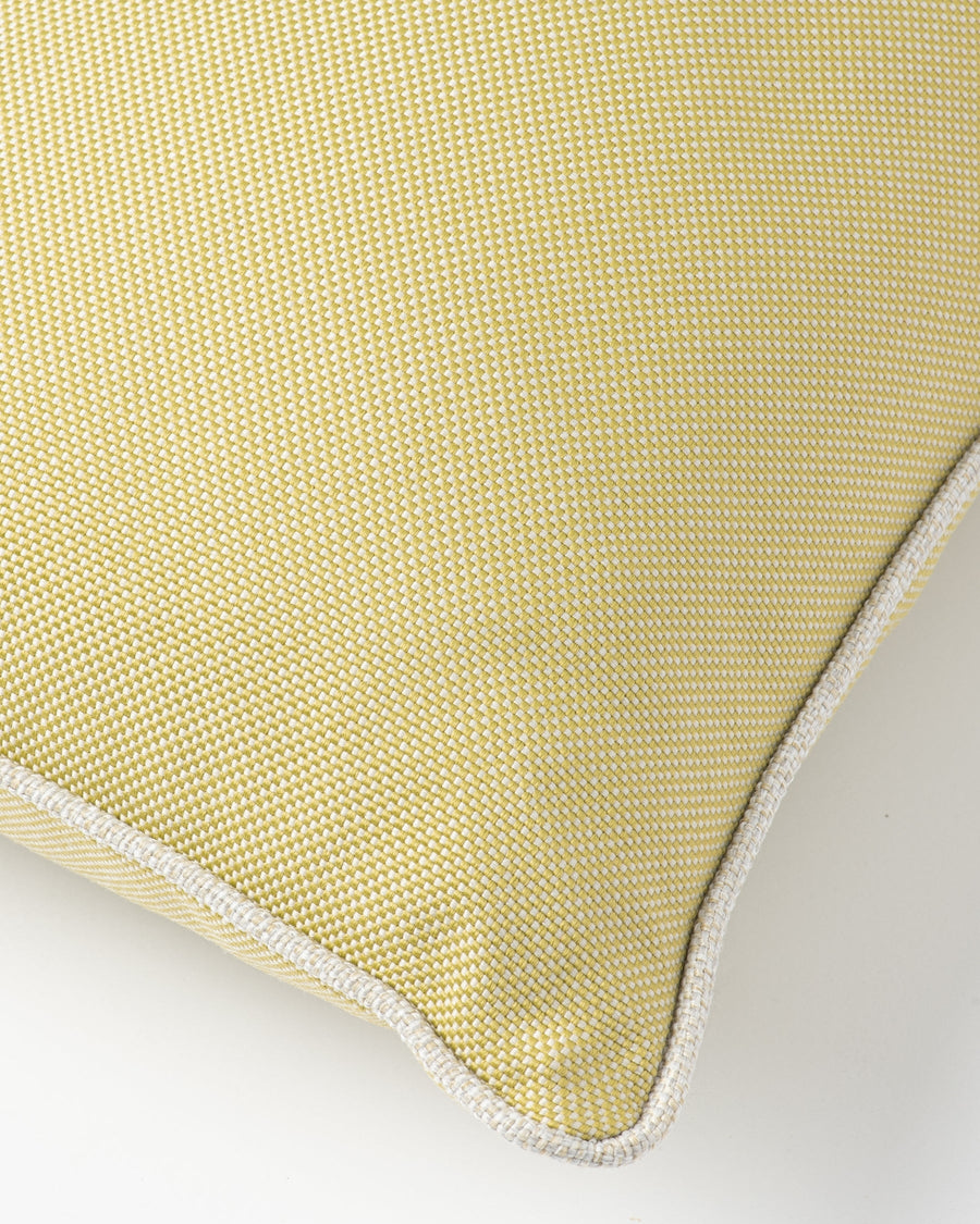 A close-up of a textured yellow-green throw pillow with a white contrast piped edge, shown on a light gray background.