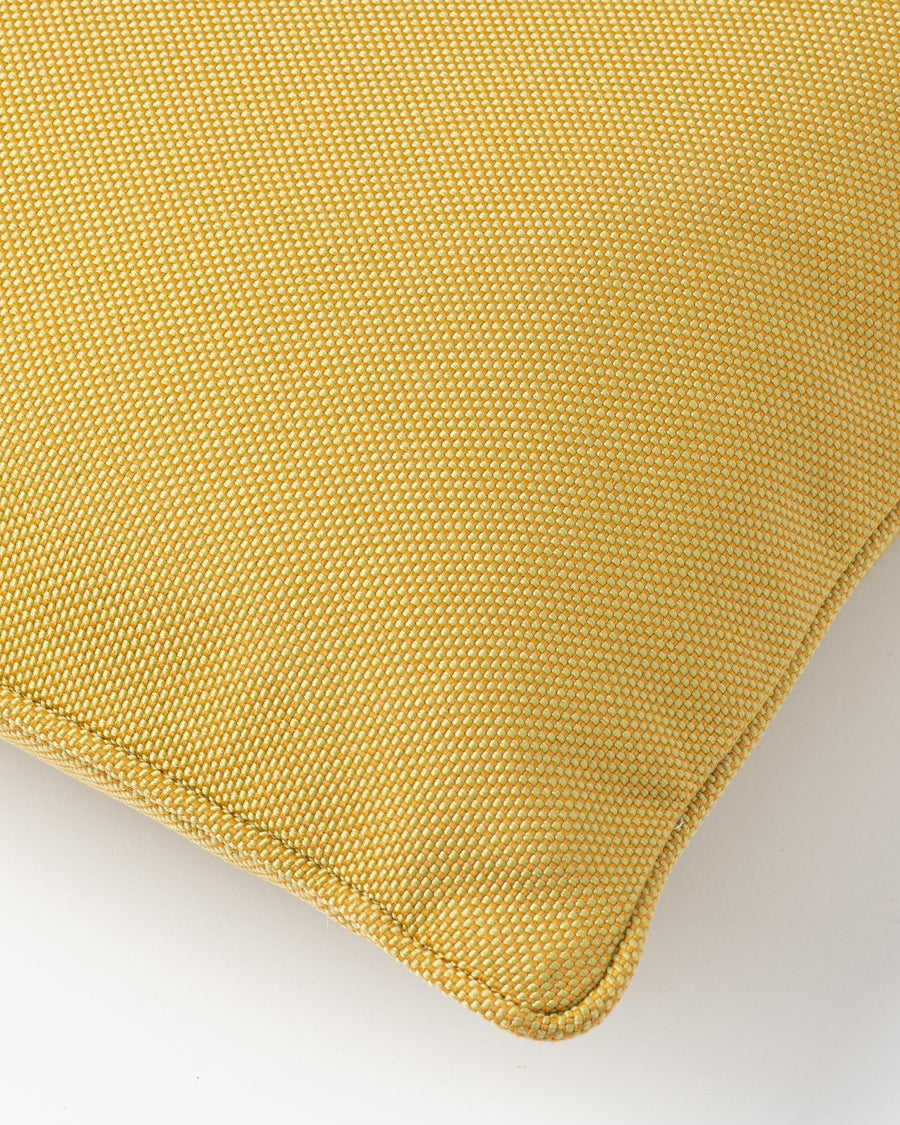 A close-up of a mustard yellow woven throw pillow corner showing the textured fabric and neat stitched edge against a plain light gray background.