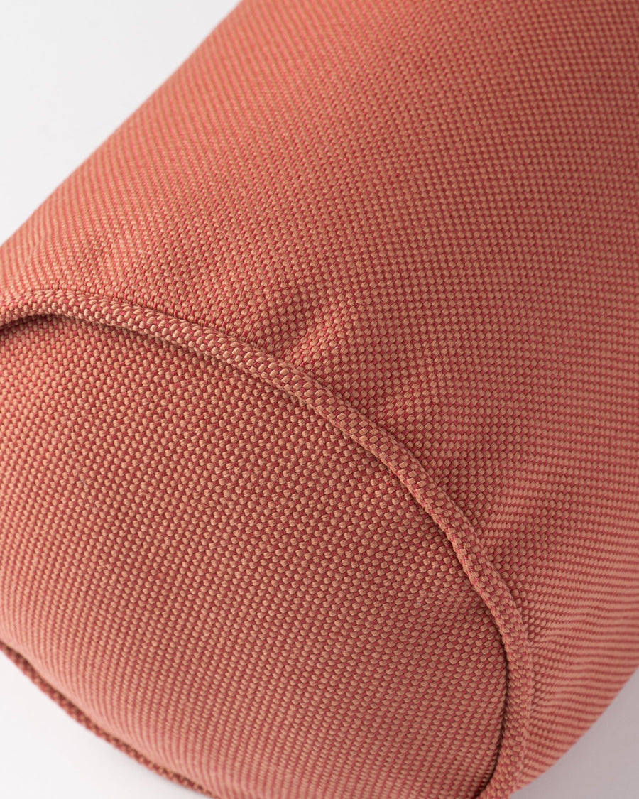 Close-up of a cylindrical fabric item in a muted terracotta or dusty rose color, showing the woven texture and curved seam against a plain light grey background.