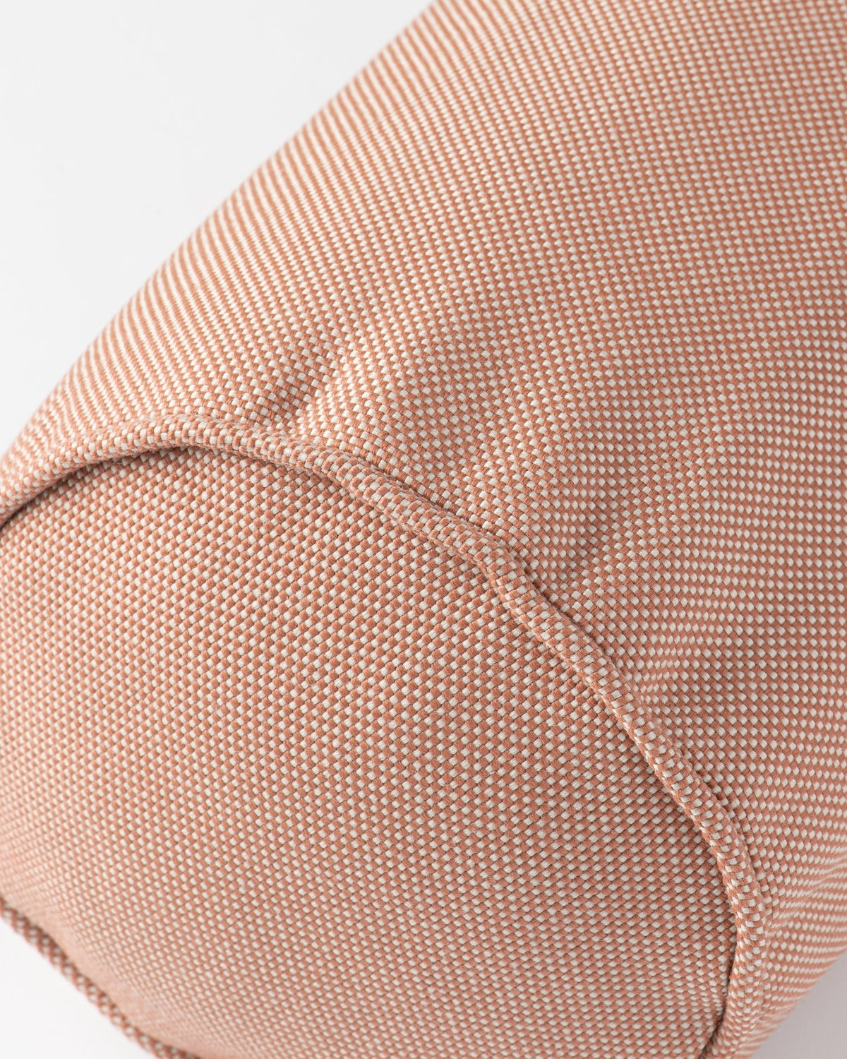 Close-up of a dusty pink textured fabric with a fine woven pattern and a curved seam, set against a plain light grey background.