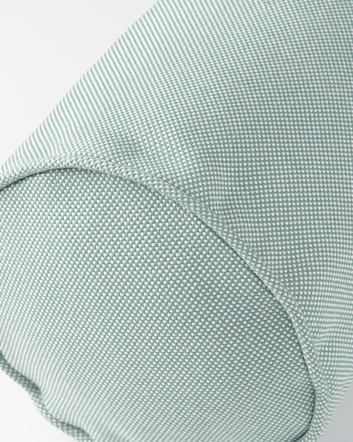 Close-up of a textured fabric cushion in a pale sage green color, showing the woven material and curved seam details.