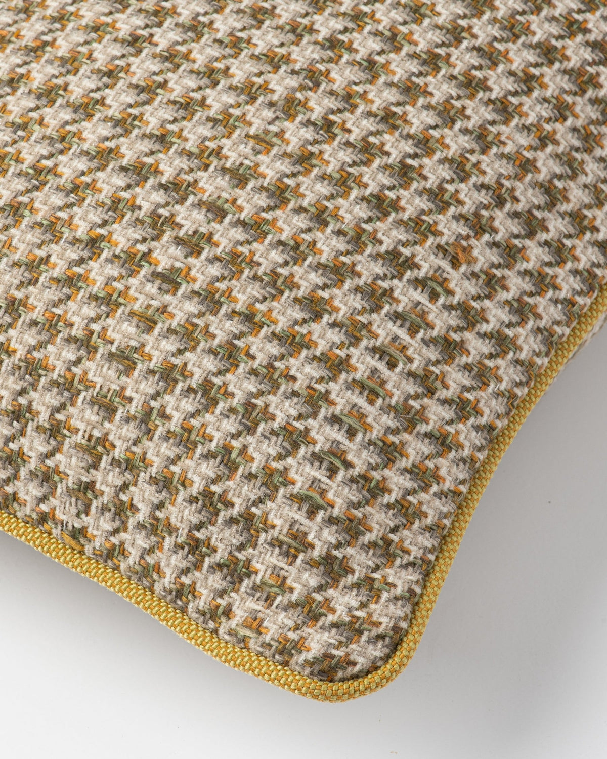 Close-up of a woven throw pillow cover featuring a textured houndstooth pattern in beige, brown, and muted green, finished with a contrasting yellow-gold piped edge.