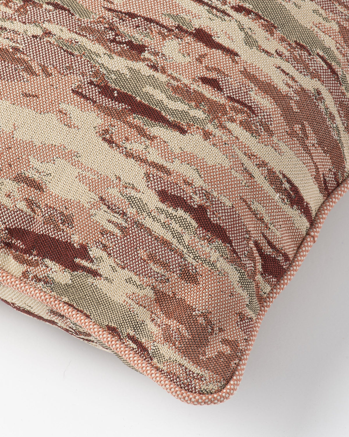 Close-up of a woven throw pillow showing a camouflage pattern in shades of beige, brown, and muted green, finished with a matching ribbed fabric piping edge.