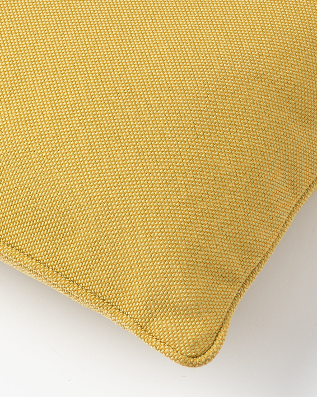 A close-up of a mustard yellow woven throw pillow corner showing the textured fabric and neat stitched edge against a plain light gray background.