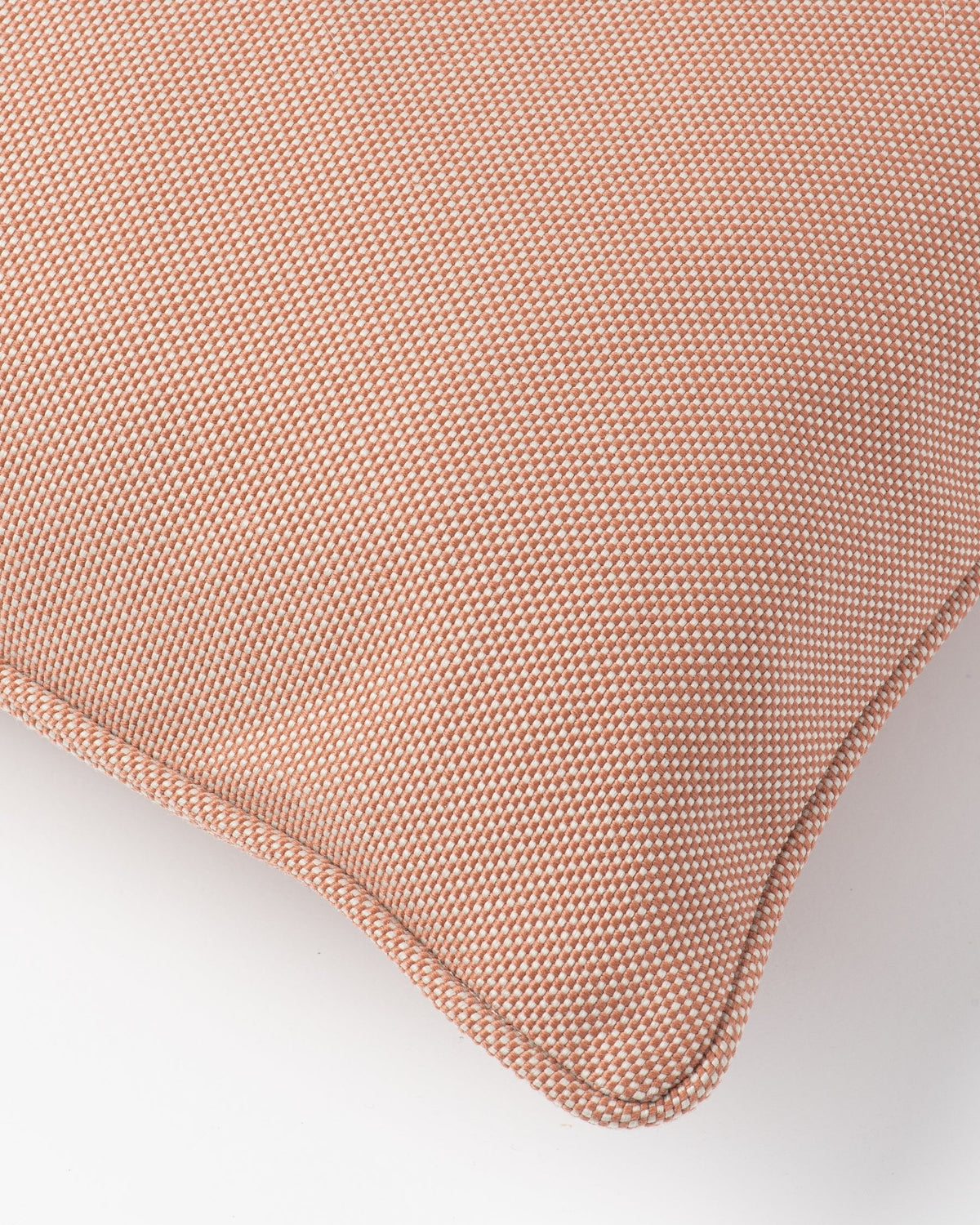 Close-up of a textured throw pillow in a dusty rose pink color, showing the woven fabric and stitched corner on a light grey background.