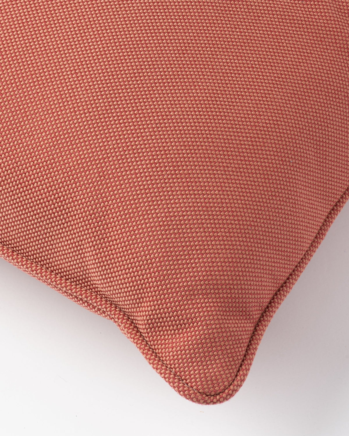 Close-up of a textured throw pillow corner in a muted terracotta or dusty rose color, showing the woven fabric and stitched edge against a plain white background.