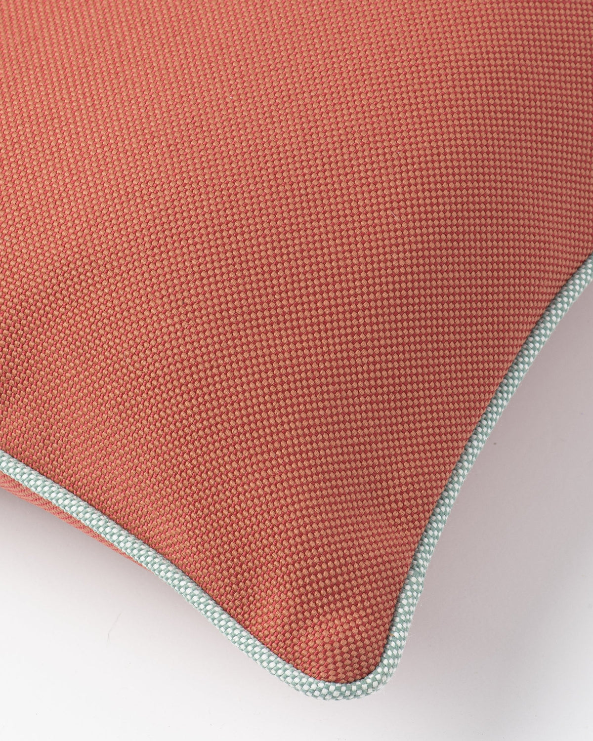 Close-up of a textured terracotta-colored cushion corner with a light blue and white patterned piped edge on a white background.