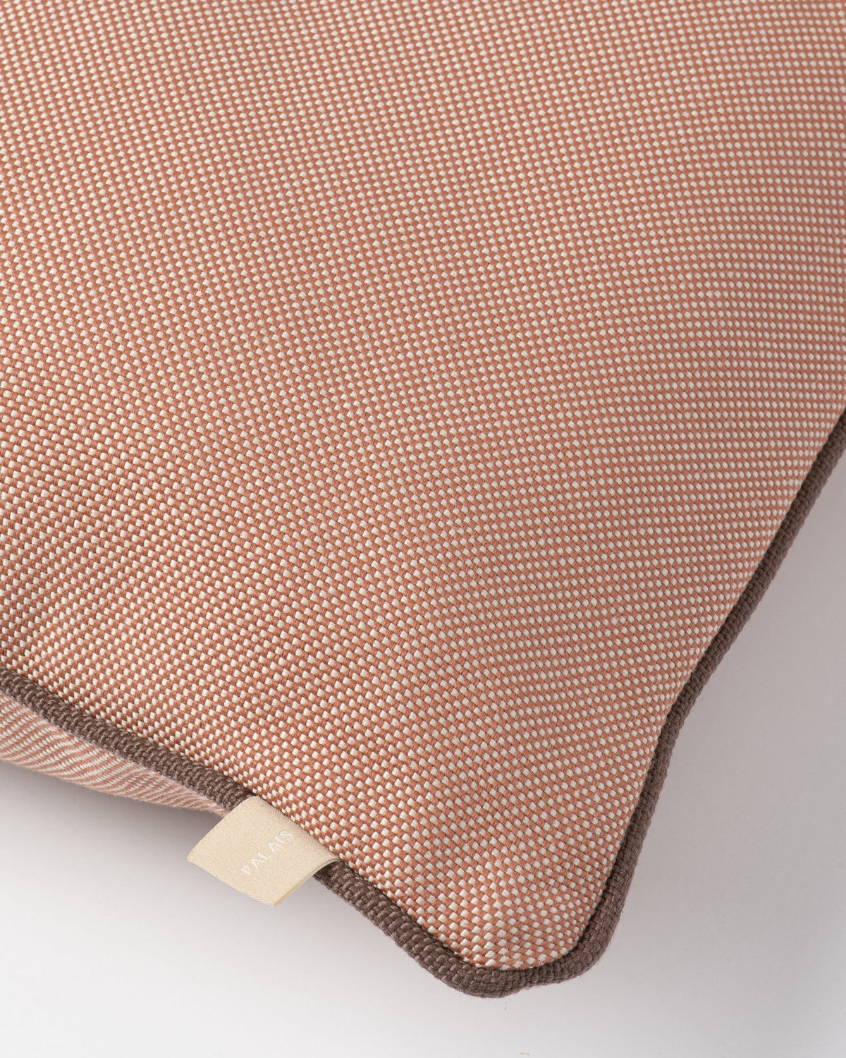 Close-up of a textured throw pillow in a dusty rose pink color with a fine woven pattern and dark brown piping along the edge.