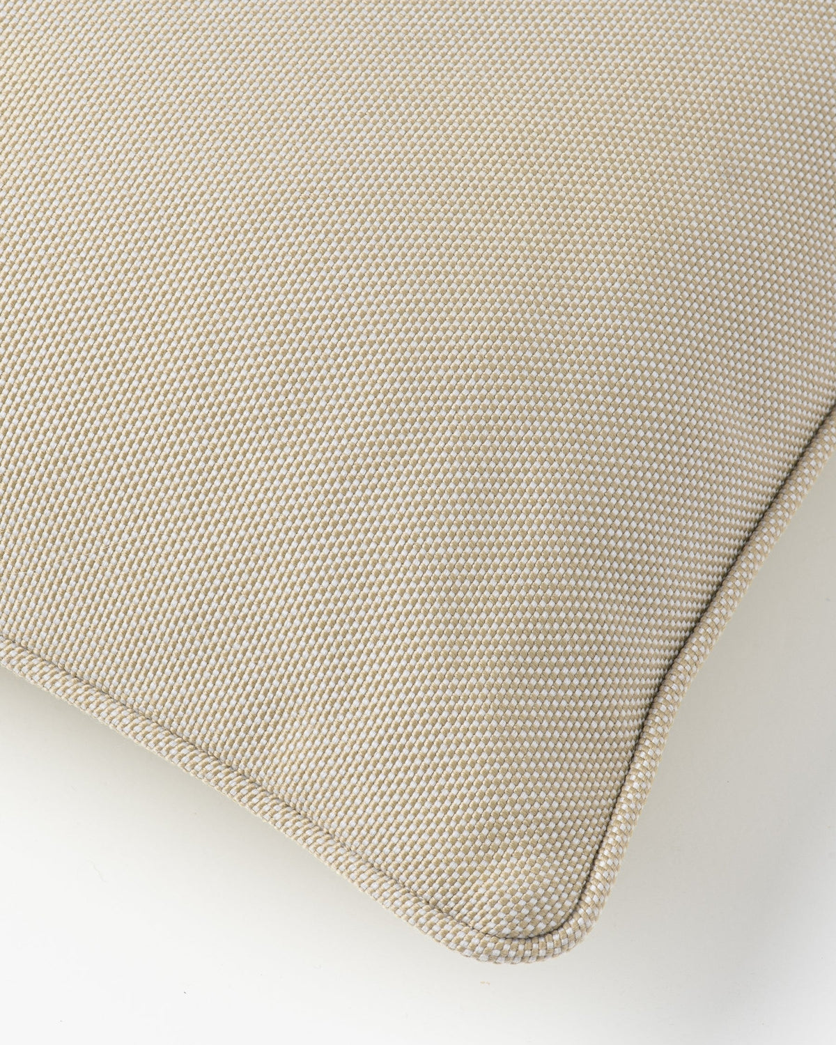 Close-up of a woven throw pillow corner in a light beige fabric, showing the texture and neat stitched edge against a light grey background.
