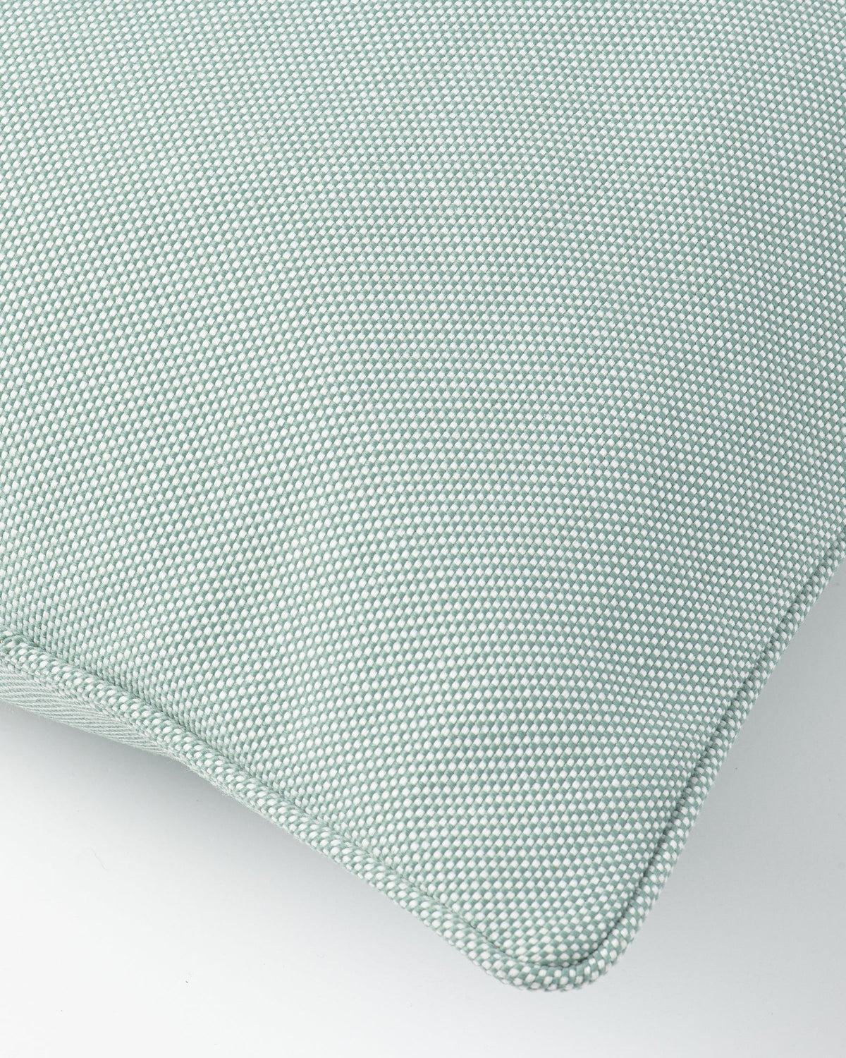 A close-up of a textured throw pillow in a light sage green color, showing the woven fabric and stitched corner seam against a plain white background.