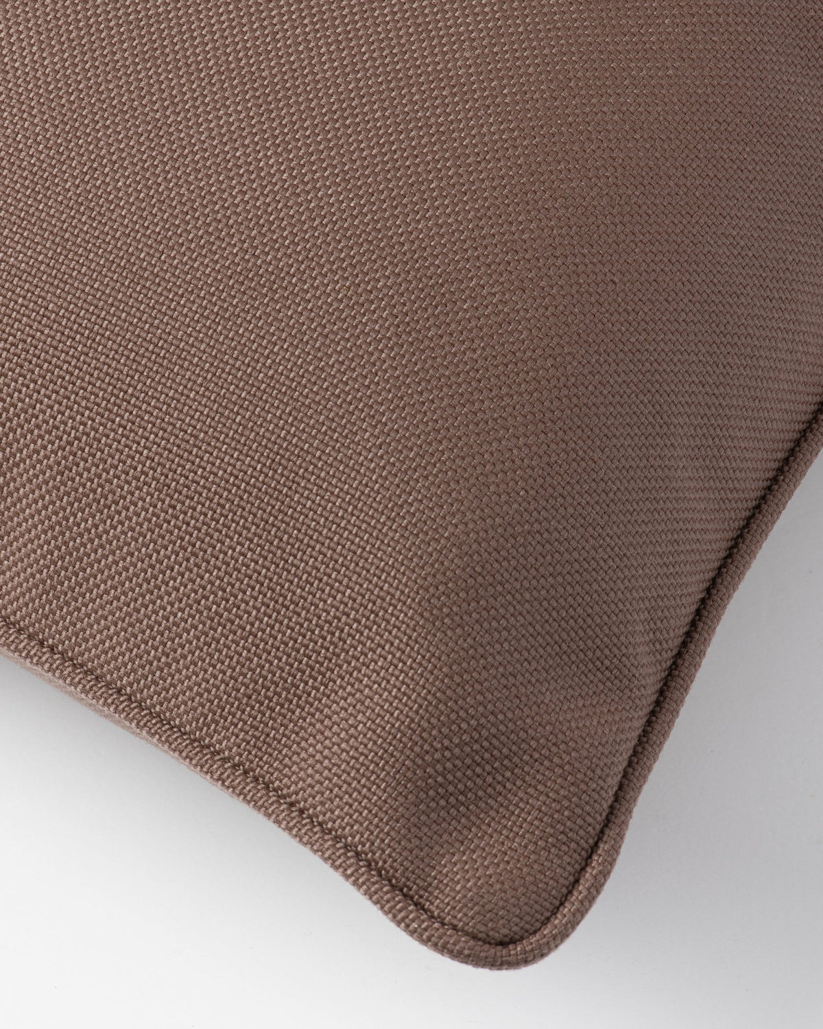 Close-up of a brown woven fabric cushion corner with a rounded stitched edge on a light gray background.