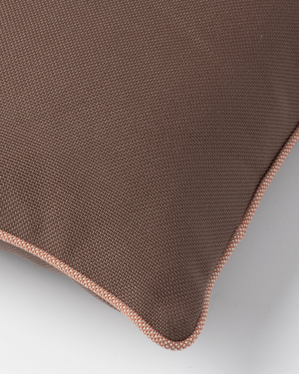 Close-up of a brown woven cushion with a contrasting dusty pink piped edge, shown on a light gray background.